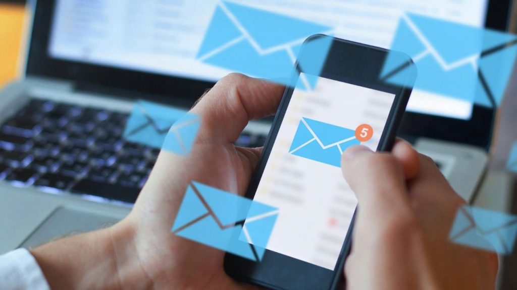 Enveloppes symbolisant des emails flottant au-dessus d'un ordinateur et d'un smartphone