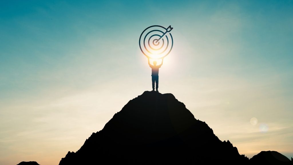 Durant votre prospection, vous devrez identifier tous les rôles qui entreront en jeu dans votre cycle de vente. Un homme tient une cible au sommet d'une montagne, avec le soleil à contrejour