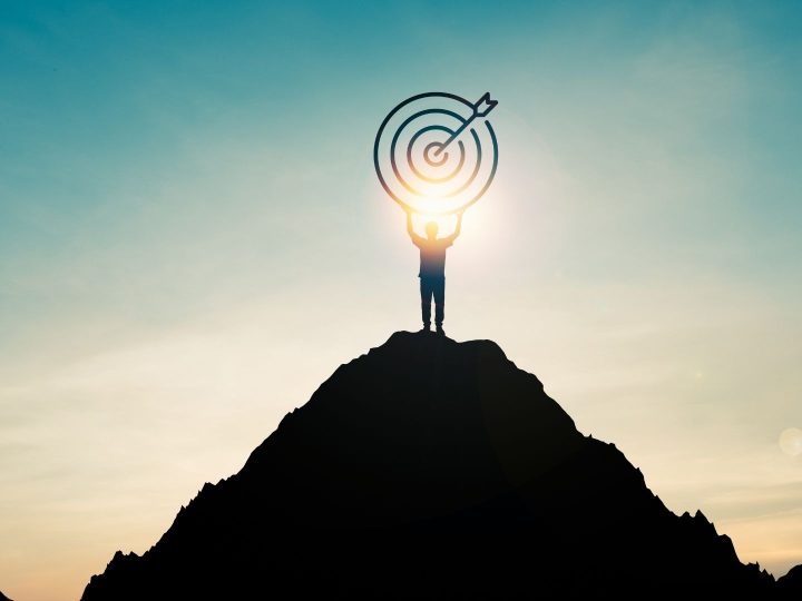 Un homme tient une cible au sommet d'une montagne, avec le soleil à contrejour