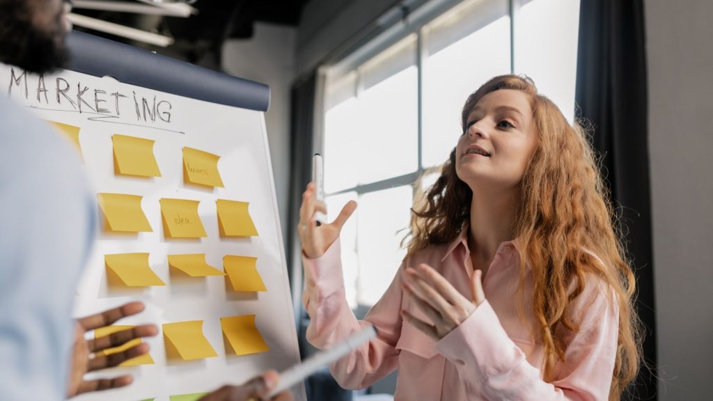 Découvrez les grandes tendances des métiers du marketing et de la communication Jeune femme devant un tableau rempli de post échangeant avec une autre personne