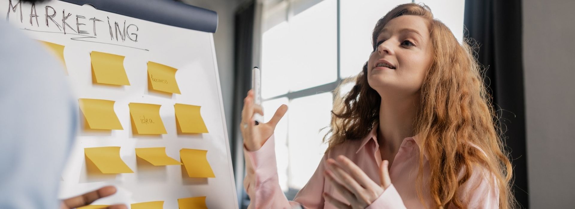Découvrez les grandes tendances des métiers du marketing et de la communication Jeune femme devant un tableau rempli de post échangeant avec une autre personne