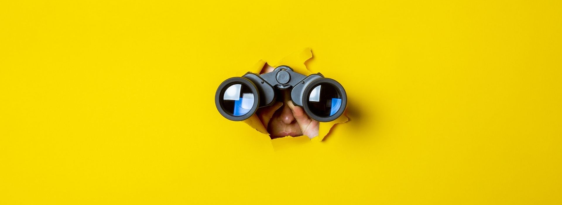 La phase de découverte est cruciale pour optimiser la gestion d’un deal et ainsi maximiser les chances de signer une vente. Des jumelles retenues par une main, sur un fond jaune