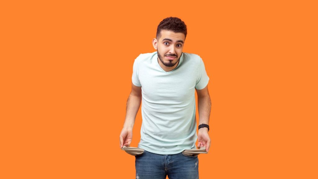 comment les marques s’adaptent-elles à la réalité économique des ménages ? Verticale de l'homme inquiet frustré de brunette tournant dehors des poches vides. coup de studio d'intérieur d'isolement sur le fond orange