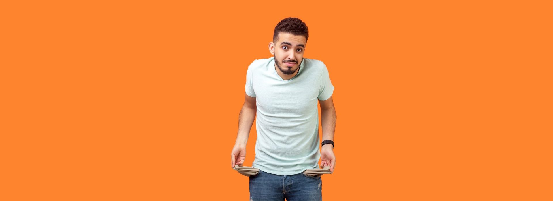 comment les marques s’adaptent-elles à la réalité économique des ménages ? Verticale de l'homme inquiet frustré de brunette tournant dehors des poches vides. coup de studio d'intérieur d'isolement sur le fond orange