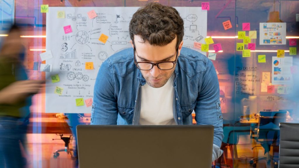 Homme travaillant dans un bureau créatif à l’aide de son ordinateur et personnes se déplaçant en arrière-plan