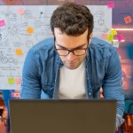 Homme travaillant dans un bureau créatif à l’aide de son ordinateur et personnes se déplaçant en arrière-plan