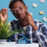 jeune adulte epuisé et pensif avec un carton contenant ses affaires professionelles posées sur le bureau et des post-it sur le mur