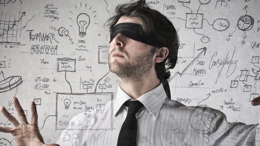 le rapport « Time to Change the Way We Work » qui en résulte a mis en évidence un écart important entre les perceptions des professionnels clés pour leur organisation dans la nouvelle ère du travail hybride. Hommes en costume cravate avec un bandeau sur les yeux devant un tableau de concepts