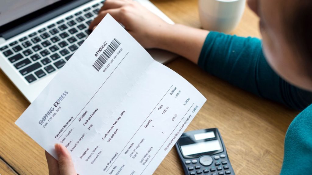 Femme tenant une fiche de paie devant un ordinateur