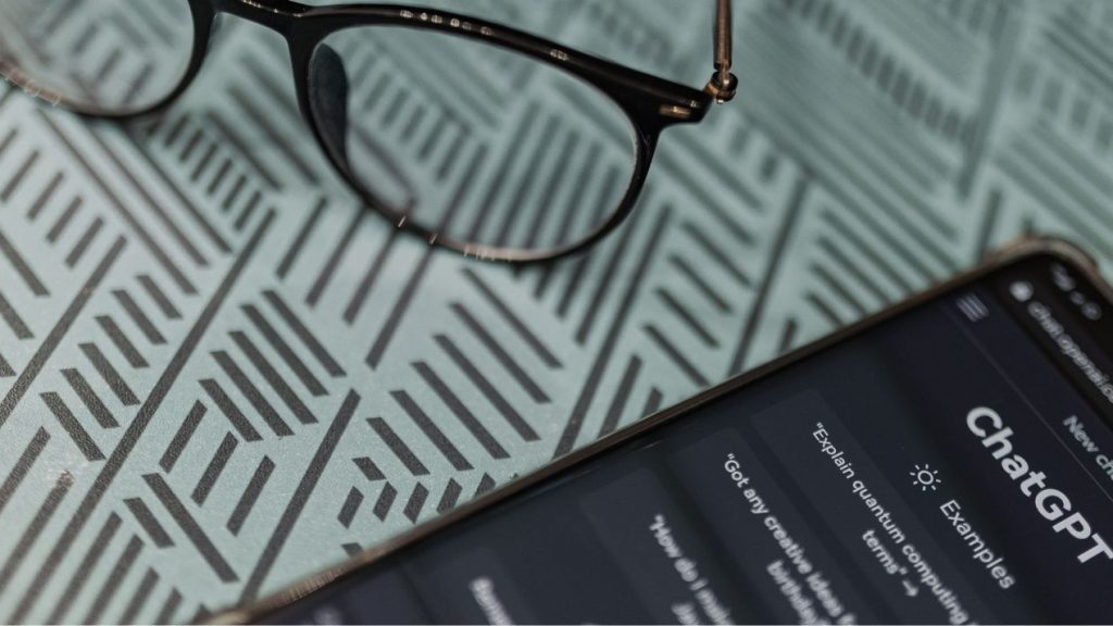 L'Académie du Newbiz lance une nouvelle formation : « Prompt Booster : l'art de briefer ChatGPT » Paire de lunettes à côté d'un téléphone portable sur l'appli ChatGPT